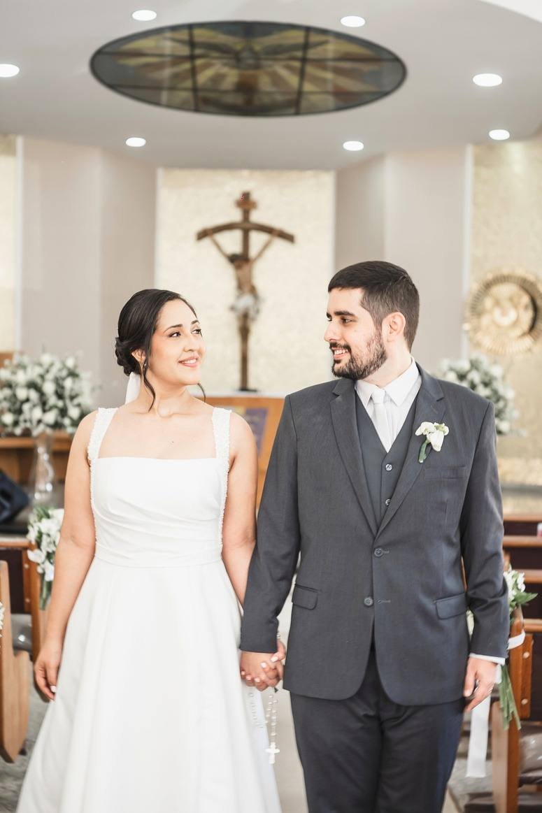 Noivos de mãos dadas sorriem um para o outro dentro da igreja